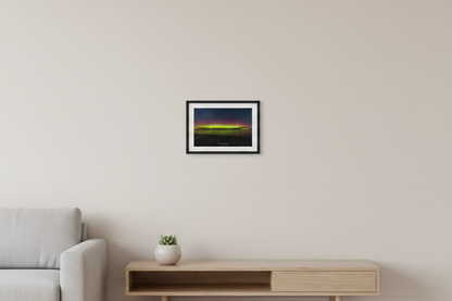 Small fine art landscape print of vivid yellow-green aurora band with crimson red pillars reflecting over Lake Michigan from Glen Haven beach with dark sandy foreground and star-filled sky March 14 2023 displayed in modern living room