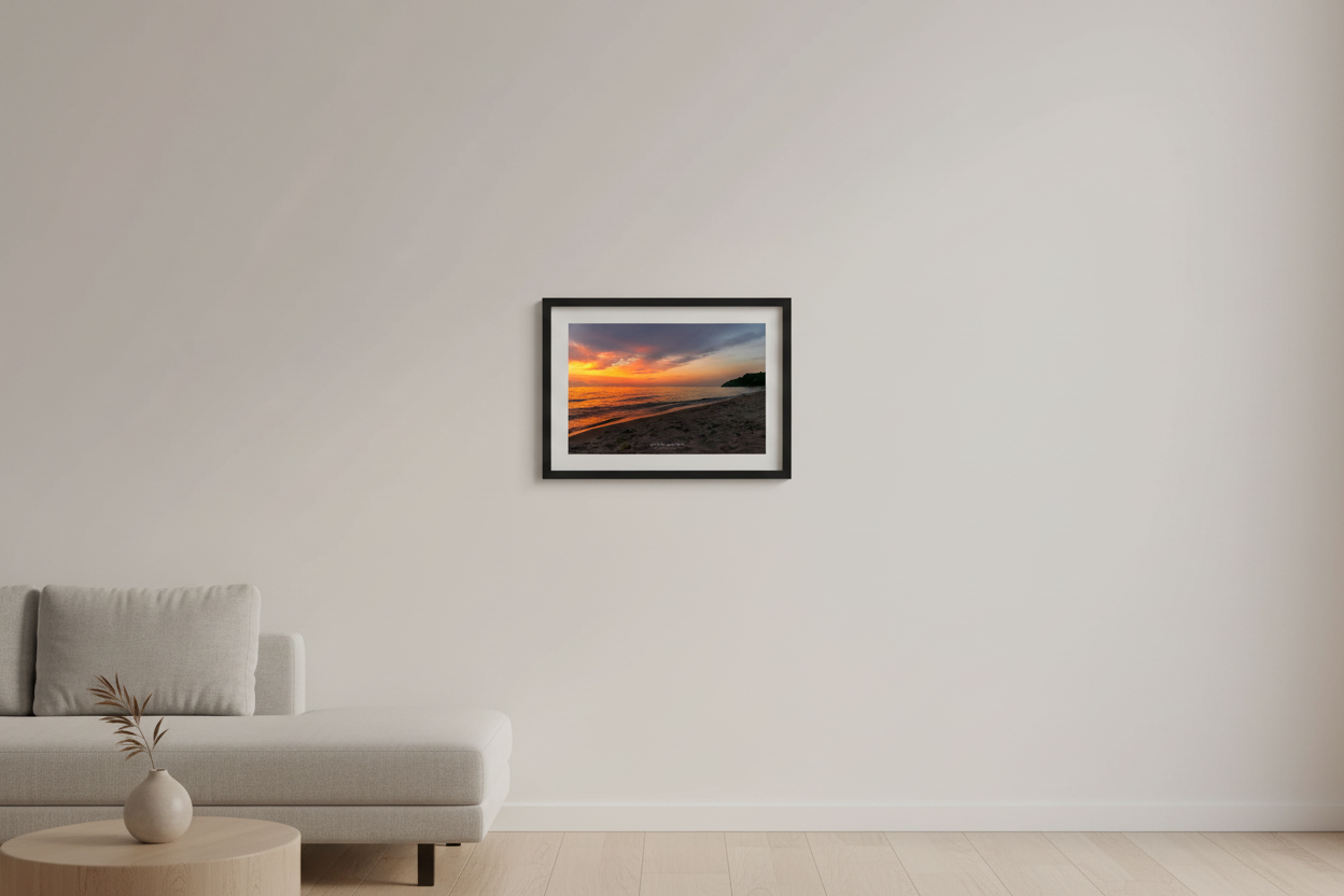 Small fine art landscape print of a blazing orange sunset over Lake Michigan with sandy beach foreground and dark tree-covered headland silhouette at Leland Michigan July 2024 displayed in modern living room