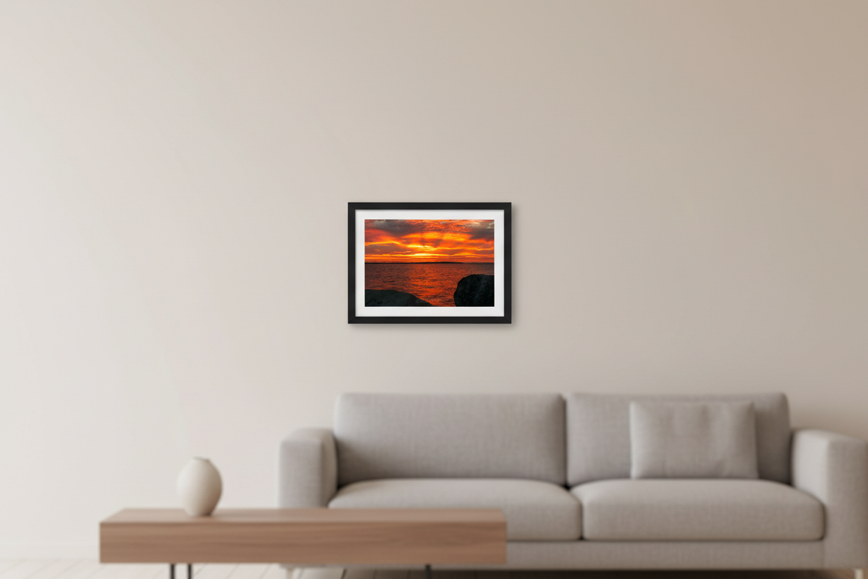 Small fine art print of blazing orange amber fire sunrise over Northport Marina with rocky foreground island silhouette and warm glowing water displayed in modern living room