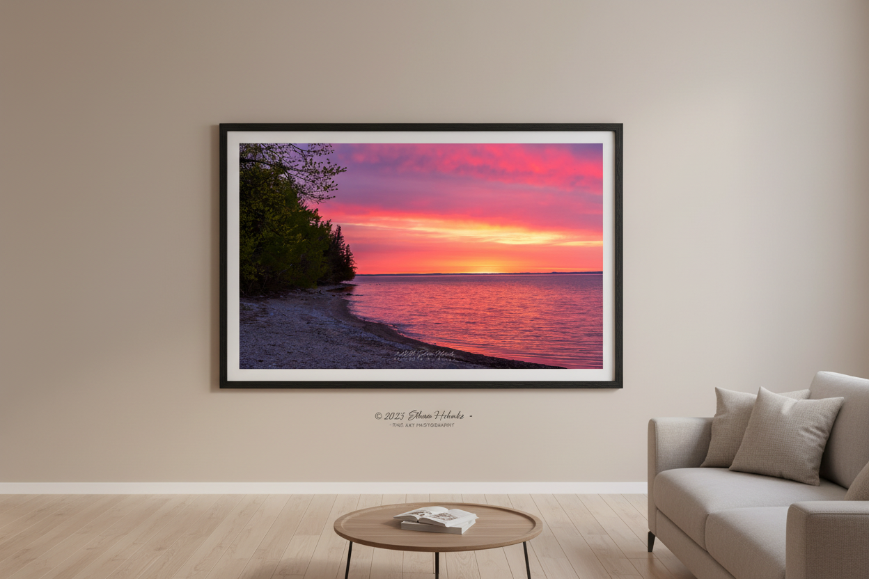 Large fine art landscape print of vivid magenta and orange Mother's Day sunrise over Grand Traverse Bay forested shoreline Michigan May 2023 displayed in modern living room