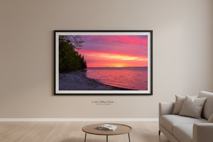 Large fine art landscape print of vivid magenta and orange Mother's Day sunrise over Grand Traverse Bay forested shoreline Michigan May 2023 displayed in modern living room