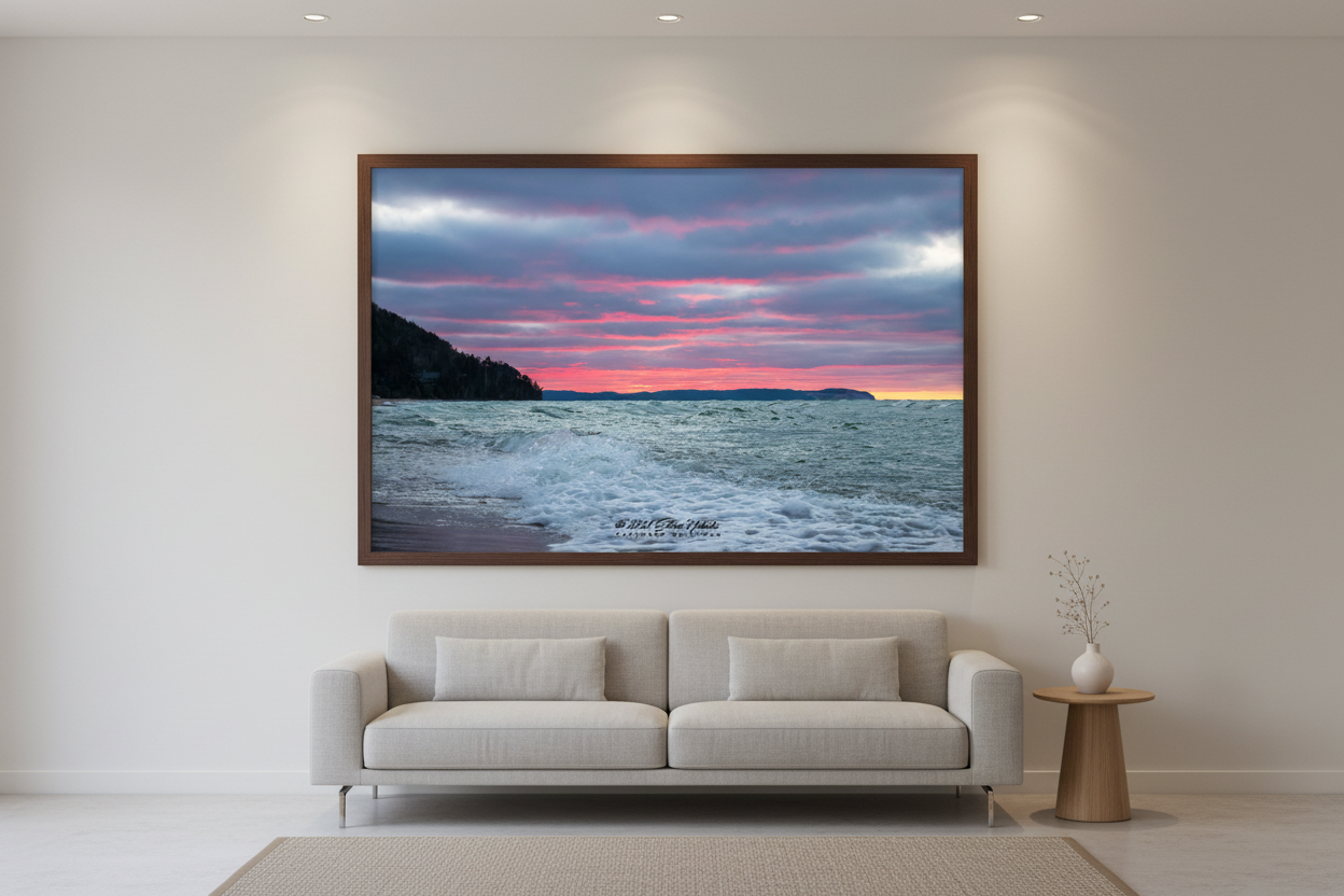 Large fine art landscape print of moody Christmas Day sunset with vivid pink and magenta bands streaking across brooding blue-grey sky with churning white-capped waves dark forested bluff silhouette and distant Sleeping Bear Dunes headland with last sliver of yellow on horizon Lake Michigan December 25 2021 displayed in modern living room