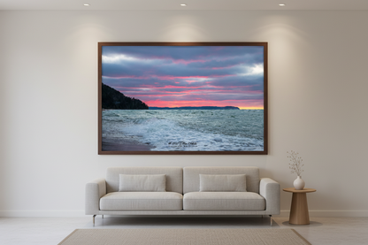 Large fine art landscape print of moody Christmas Day sunset with vivid pink and magenta bands streaking across brooding blue-grey sky with churning white-capped waves dark forested bluff silhouette and distant Sleeping Bear Dunes headland with last sliver of yellow on horizon Lake Michigan December 25 2021 displayed in modern living room