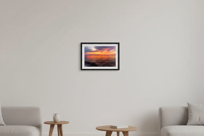 Small fine art landscape print of a fiery orange and magenta sunset over calm Lake Michigan waters with rocky shoreline foreground viewed from Leland Michigan July 2024 displayed in modern living room