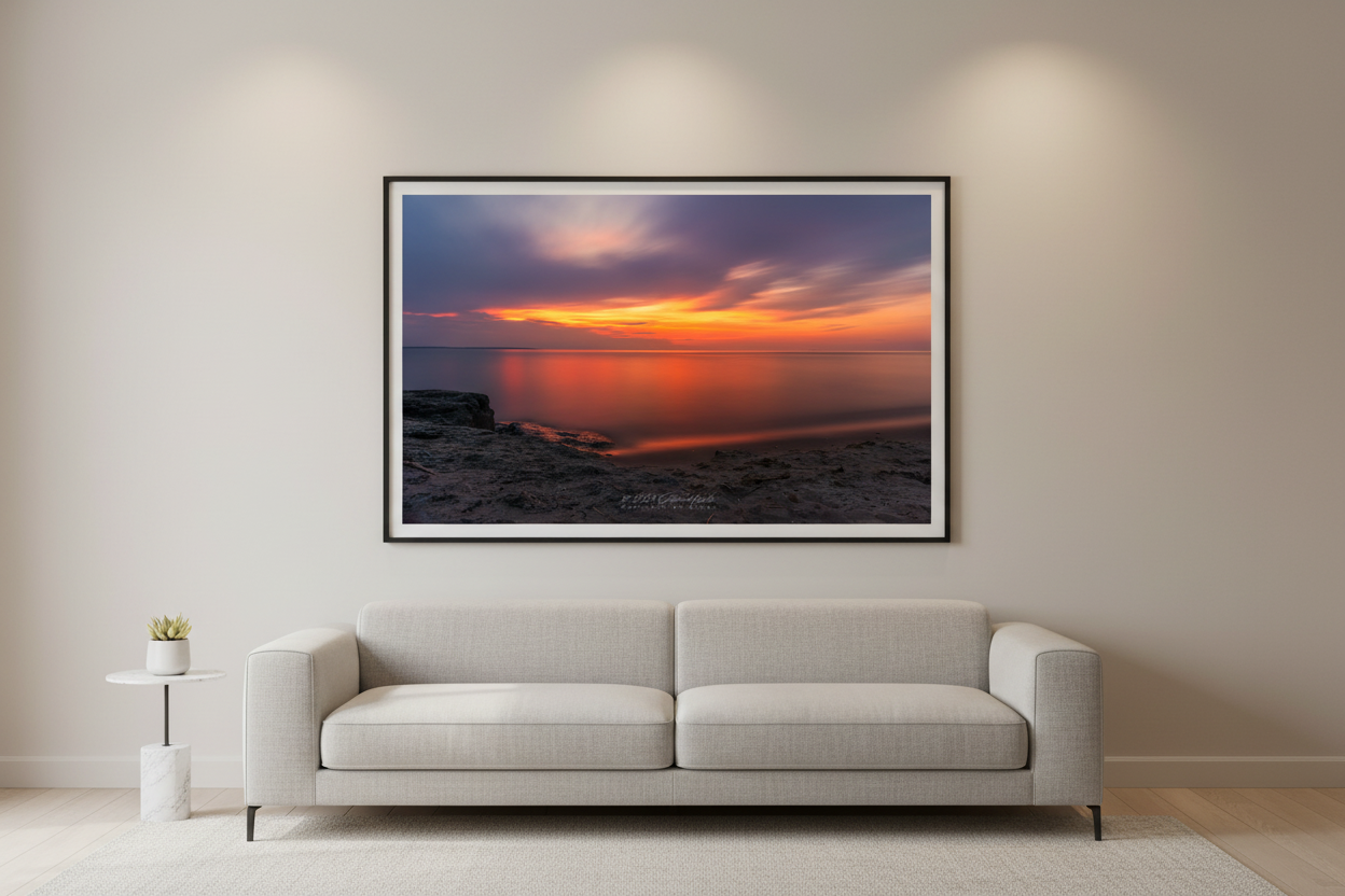 Large fine art landscape long exposure print of watercolor orange gold sunset with silky smooth water reflection and rocky shoreline on Lake Michigan July 2024 displayed in modern living room