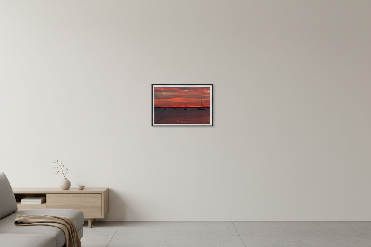 Small fine art print of blazing red fire sunrise over Northport Marina with fleet of sailboat silhouettes against intensely crimson layered sky over dark moody harbor water displayed in modern living room