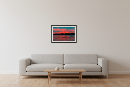 Small fine art print of Lake Leelanau fire sunset with visible golden sun orb at treeline centered L-shaped swimming dock with benches magenta pink sky teal storm clouds wide open water foreground swim rope buoy line Leland Michigan displayed in modern living room