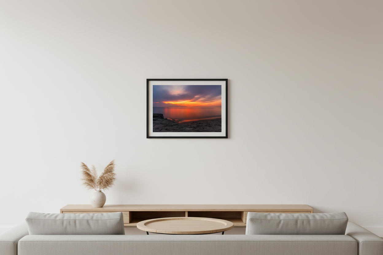 Small fine art landscape long exposure print of watercolor orange gold sunset with silky smooth water reflection and rocky shoreline on Lake Michigan July 2024 displayed in modern living room