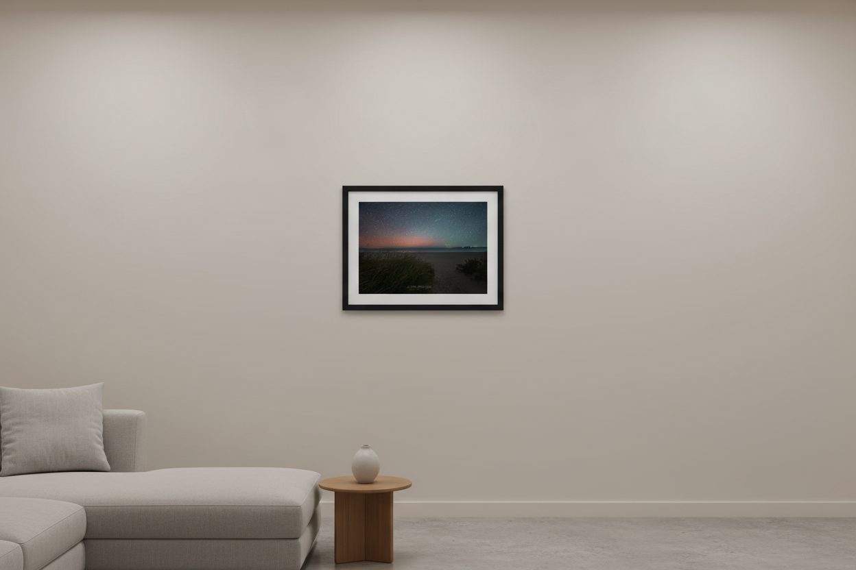 Small fine art print of aurora borealis pink red glow over Bohemian Road Beach Michigan dune grass clumps open sandy beach calm dark water distant landmass starfield sky Oct 5 2024 displayed in modern living room