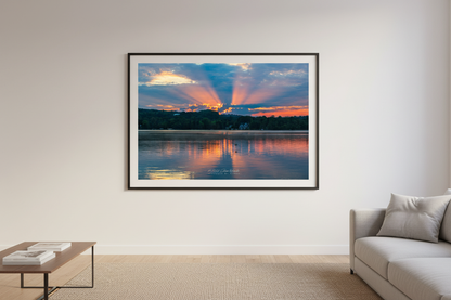 Large fine art landscape print of dramatic crepuscular rays bursting through storm clouds over glassy Lake Leelanau with warm orange horizon Michigan August 2022 displayed in modern living room