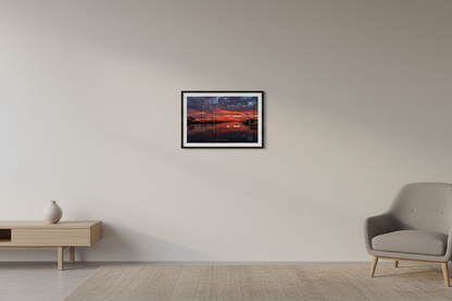 Small fine art landscape print of fiery red sunrise over Northport Marina sailboats with glassy water reflection displayed in modern living room