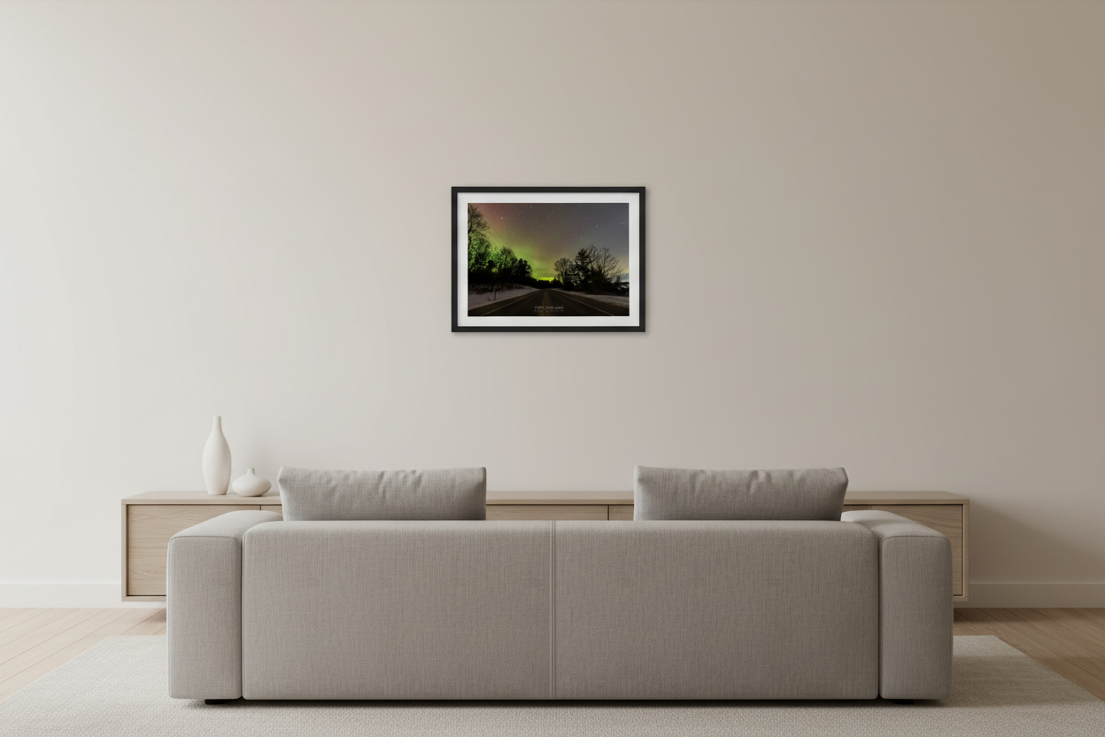Small fine art landscape print of vivid green and yellow Northern Lights aurora over M-22 road with silhouetted trees and snow-covered shoulders in Leelanau County Michigan February 27 2023 displayed in modern living room