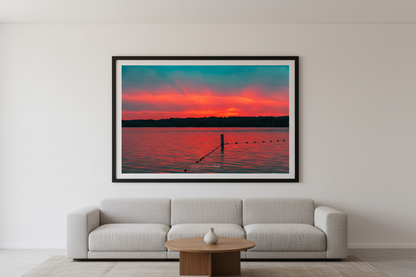 Large fine art print of Lake Leelanau fire sunset afterglow with single wooden swim rope post V-shaped buoy lines vivid saturated teal sky sweeping crimson orange cloud band golden afterglow at treeline vast open water foreground no dock Leland Michigan displayed in modern living room