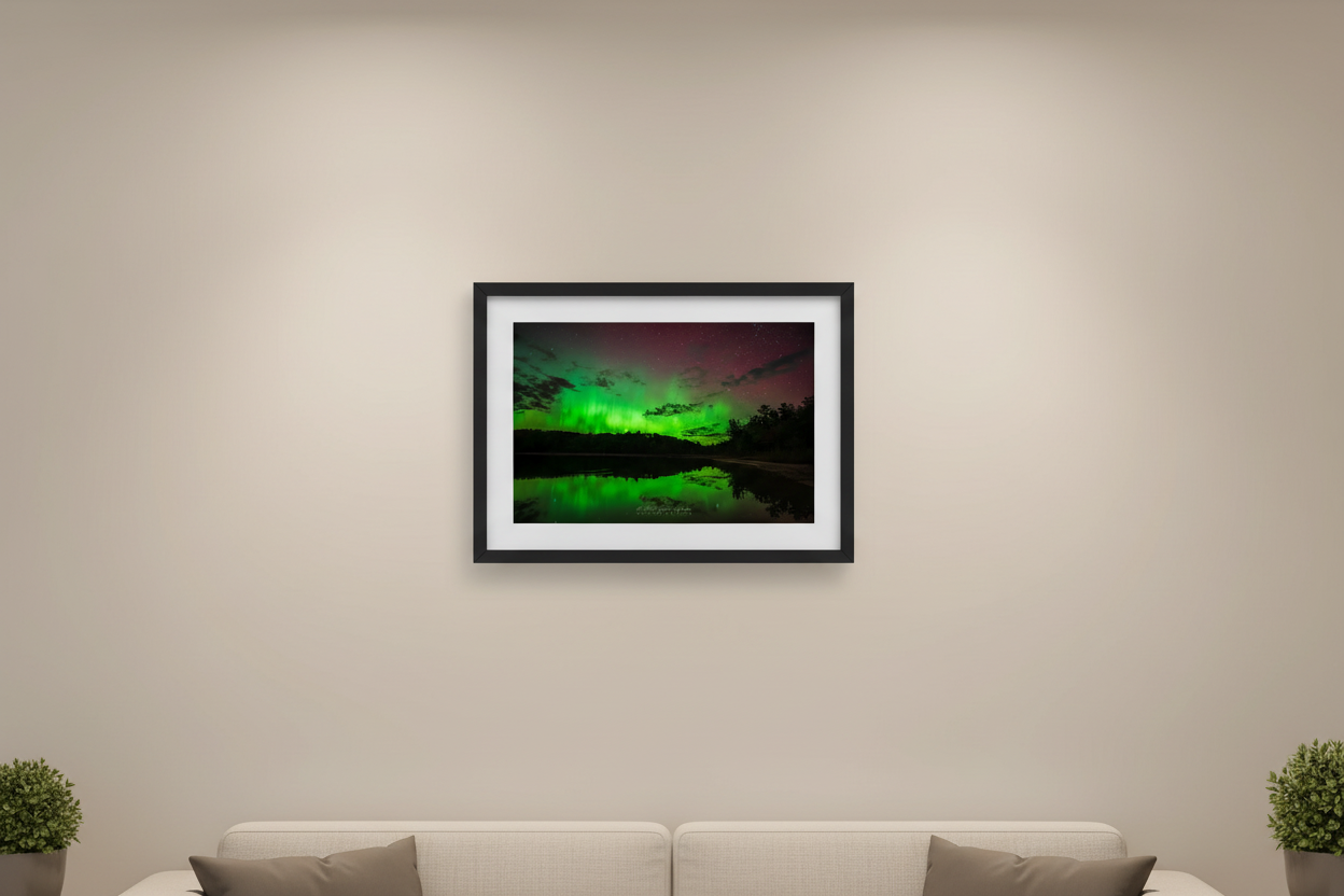 Small fine art landscape print of vivid electric green aurora curtains reflected in glassy Shell Lake with dark silhouetted tree line and crimson red sky within Sleeping Bear Dunes National Lakeshore Michigan October 7 2024 at 10:36pm displayed in modern living room