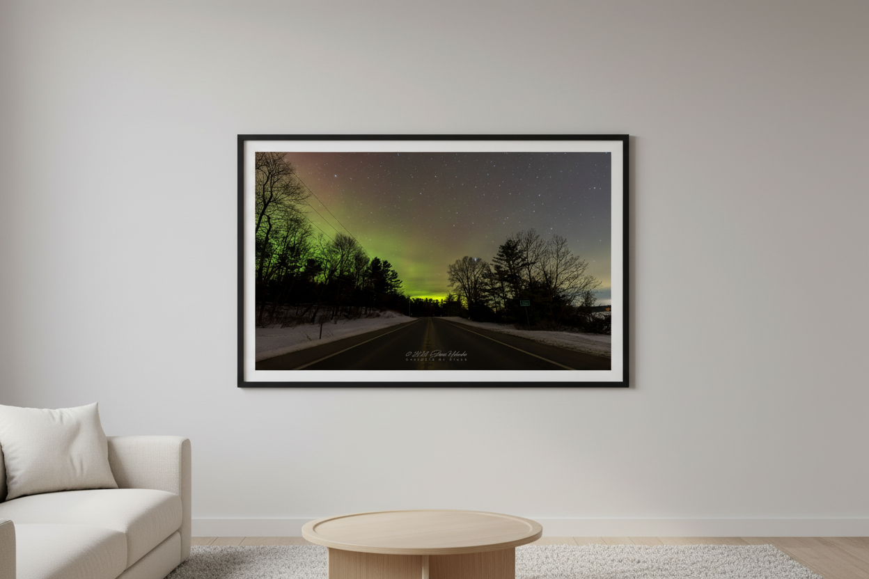 Large fine art landscape print of vivid green and yellow Northern Lights aurora over M-22 road with silhouetted trees and snow-covered shoulders in Leelanau County Michigan February 27 2023 displayed in modern living room