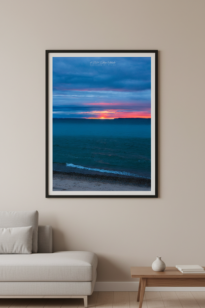 Large fine art portrait print of a moody long exposure sunset afterglow with fiery orange horizon splitting the Manitou Islands over teal blue Lake Michigan from Leland Michigan April 4 2024 displayed in modern living room