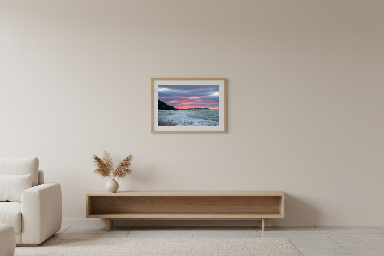 Small fine art landscape print of moody Christmas Day sunset with vivid pink and magenta bands streaking across brooding blue-grey sky with churning white-capped waves dark forested bluff silhouette and distant Sleeping Bear Dunes headland with last sliver of yellow on horizon Lake Michigan December 25 2021 displayed in modern living room